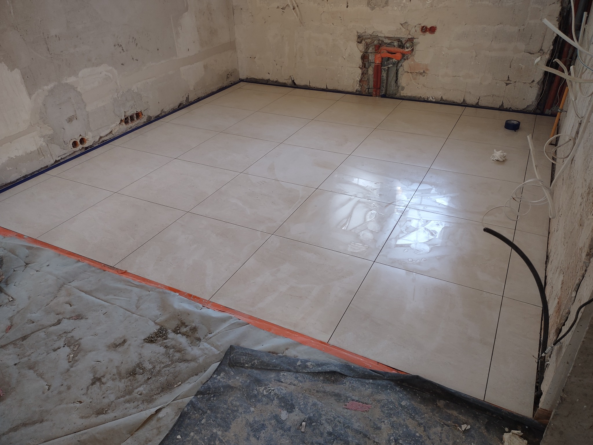 Ułożona podłoga z płytek ceramicznych w trakcie remontu łazienki, widoczne niezabezpieczone ściany i podłoga zabezpieczona folią malarską.
