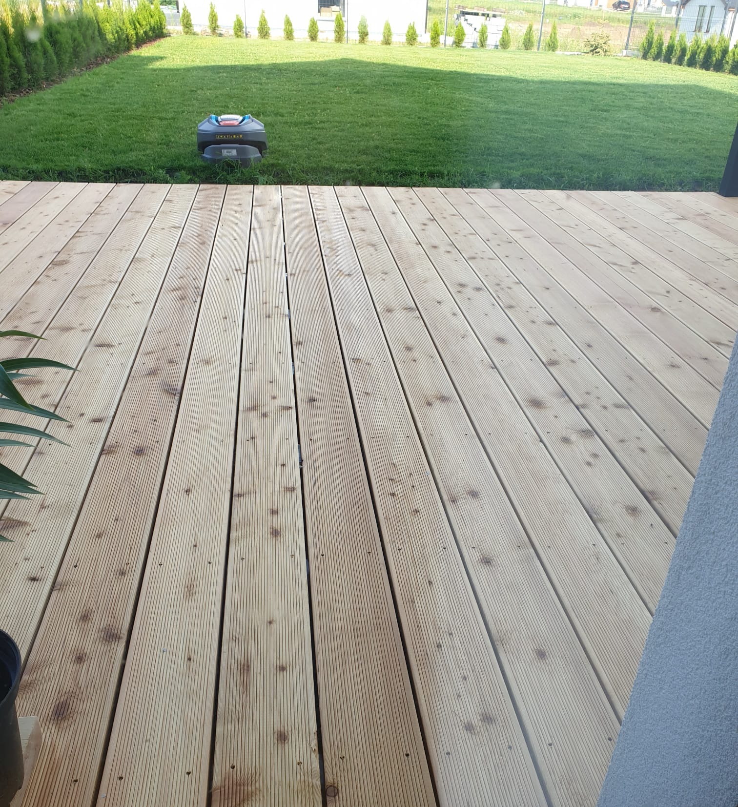 Świeżo położony, drewniany taras w Elblągu z widokiem na trawnik i automatyczną kosiarkę.