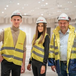GRUPA SAFETOM SPÓŁKA Z OGRANICZONĄ ODPOWIEDZIALNOŚCIĄ - Trzy osoby w odzieży roboczej i kaskach z logo SAFETOM, stojące w jasnym, przestronnym wnętrzu w trakcie realizacji inwestycji.