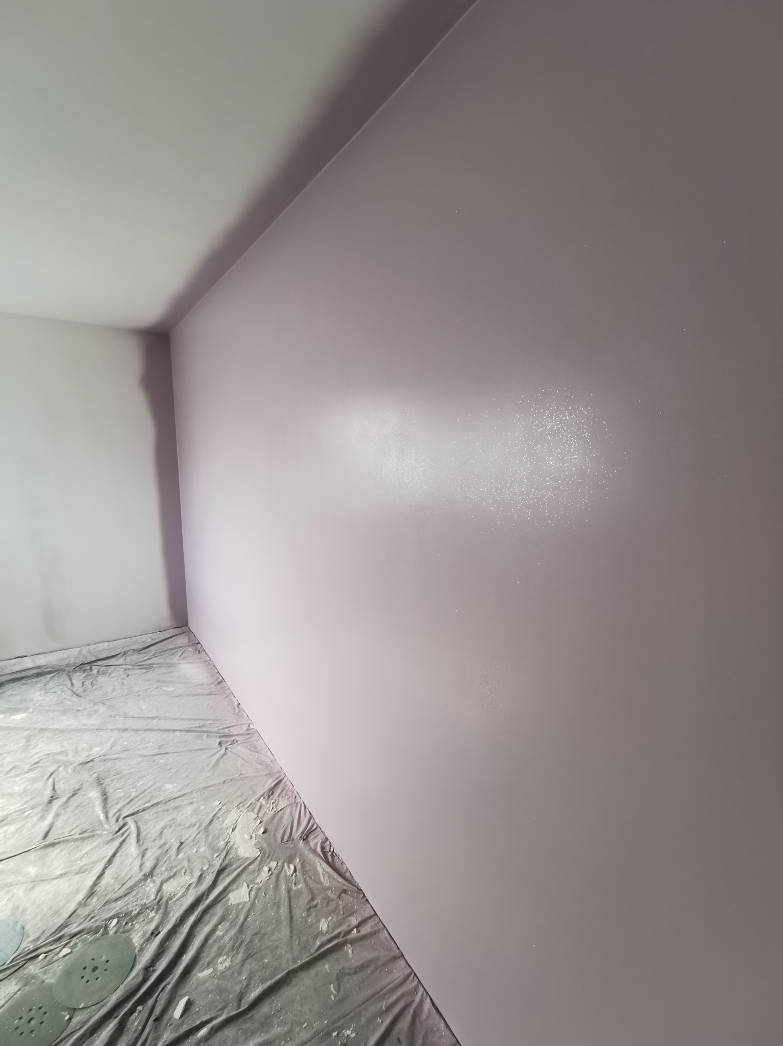 Świeżo pomalowane na liliowo ściany w rogu pokoju, podłoga zabezpieczona folią malarską z resztkami gipsu i krążkami ściernymi.