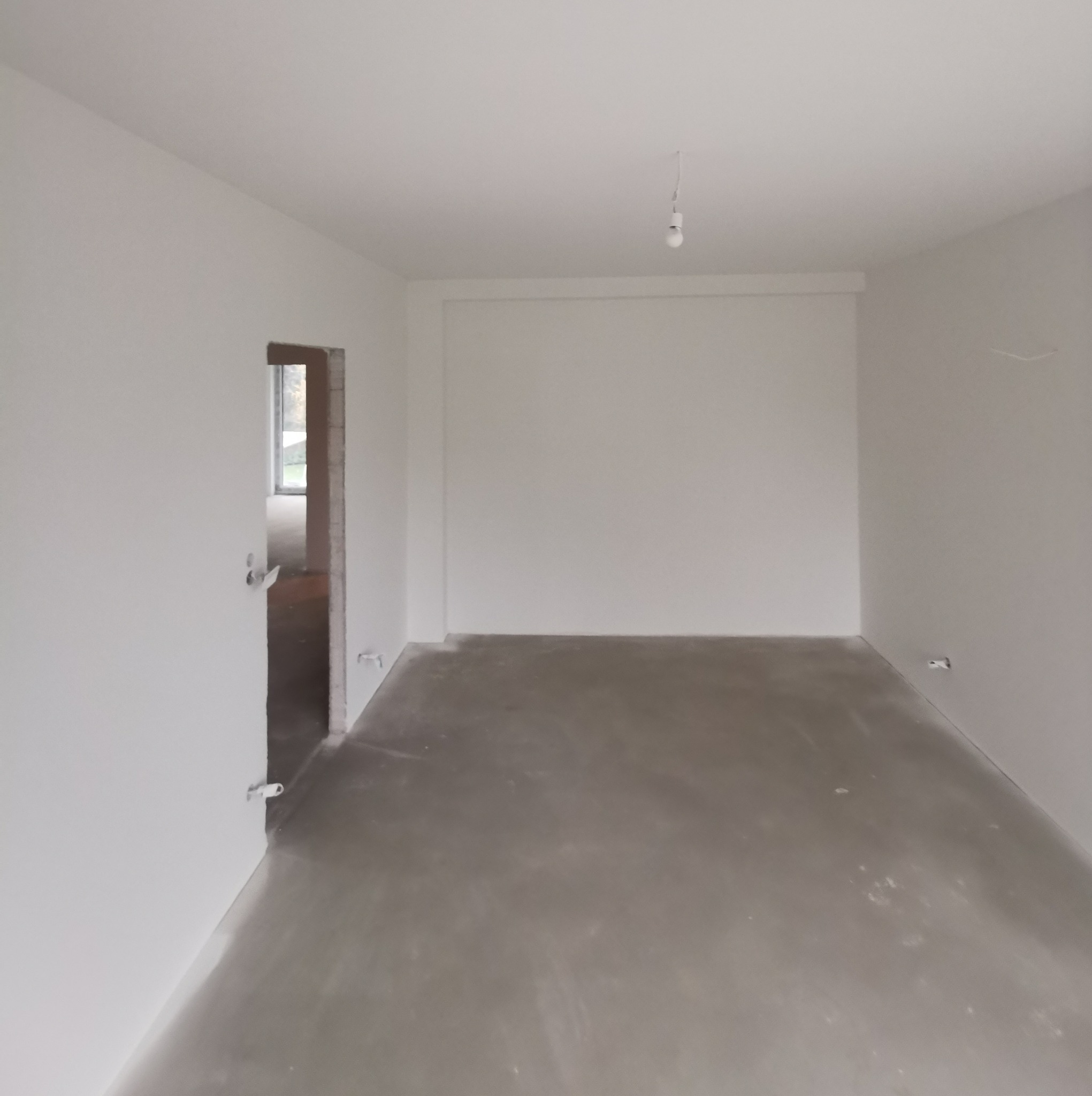 Pusty pokój po szpachlowaniu i malowaniu na biało, widoczne gniazdka elektryczne bez osłon i surowa podłoga, uchwycona z perspektywy wejścia.