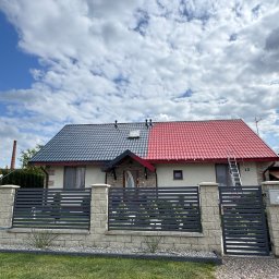 HOGAASTAR SPÓŁKA Z OGRANICZONĄ ODPOWIEDZIALNOŚCIĄ - Dom jednorodzinny z dachem pomalowanym w połowie na szaro, a w połowie na czerwono. Drabina oparta o dach. Widoczne ogrodzenie i trawnik.