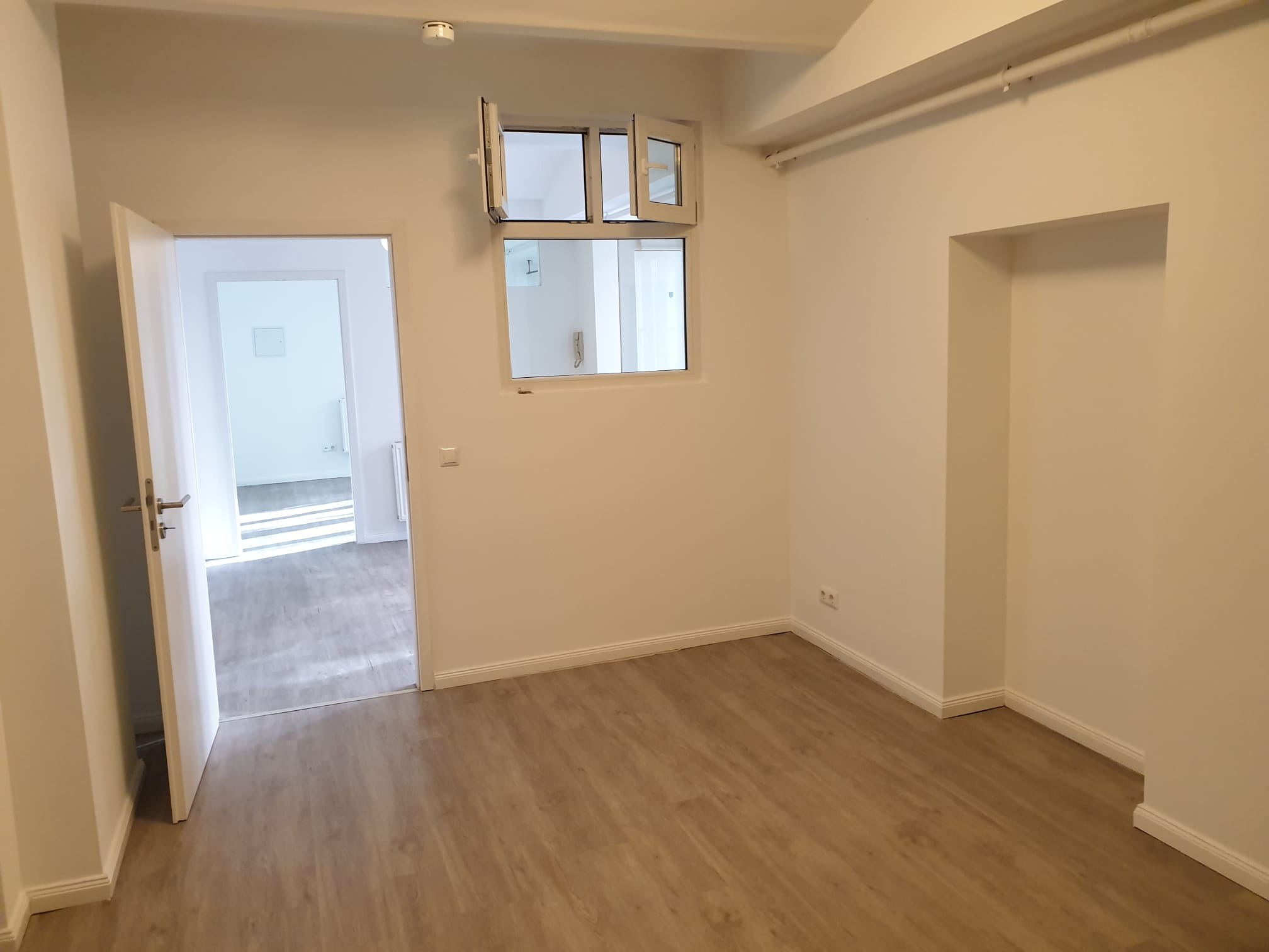 Jasne wnętrze po remoncie: podłoga z paneli, białe ściany, otwarte drzwi i okno. Minimalistyczny styl wykończenia, świeżo odnowione pomieszczenie.