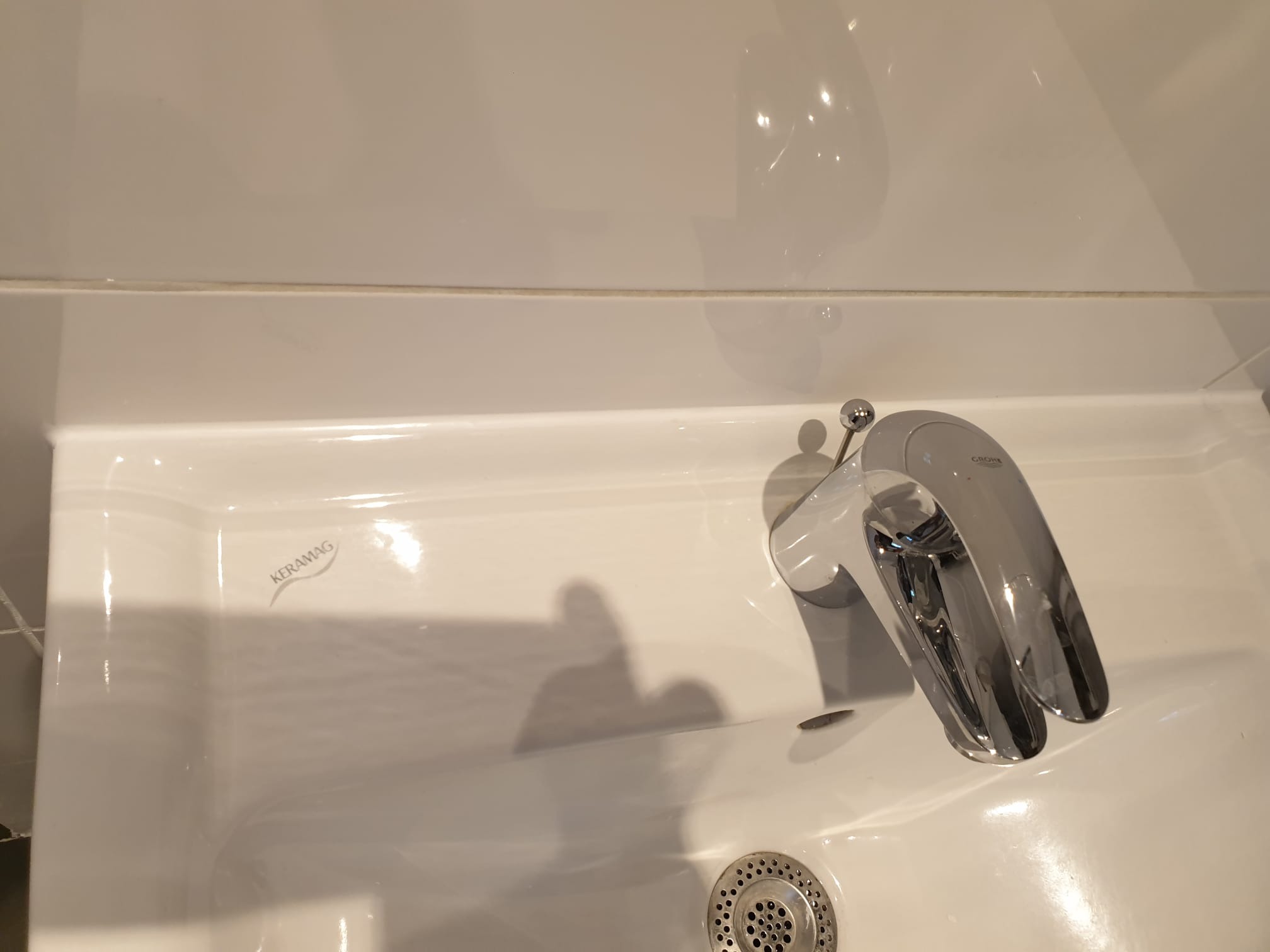 Biała umywalka Keramag z chromowaną baterią Grohe, widoczny odpływ i fragment białych płytek. Minimalistyczny design łazienki, czysty i nowoczesny wygląd.