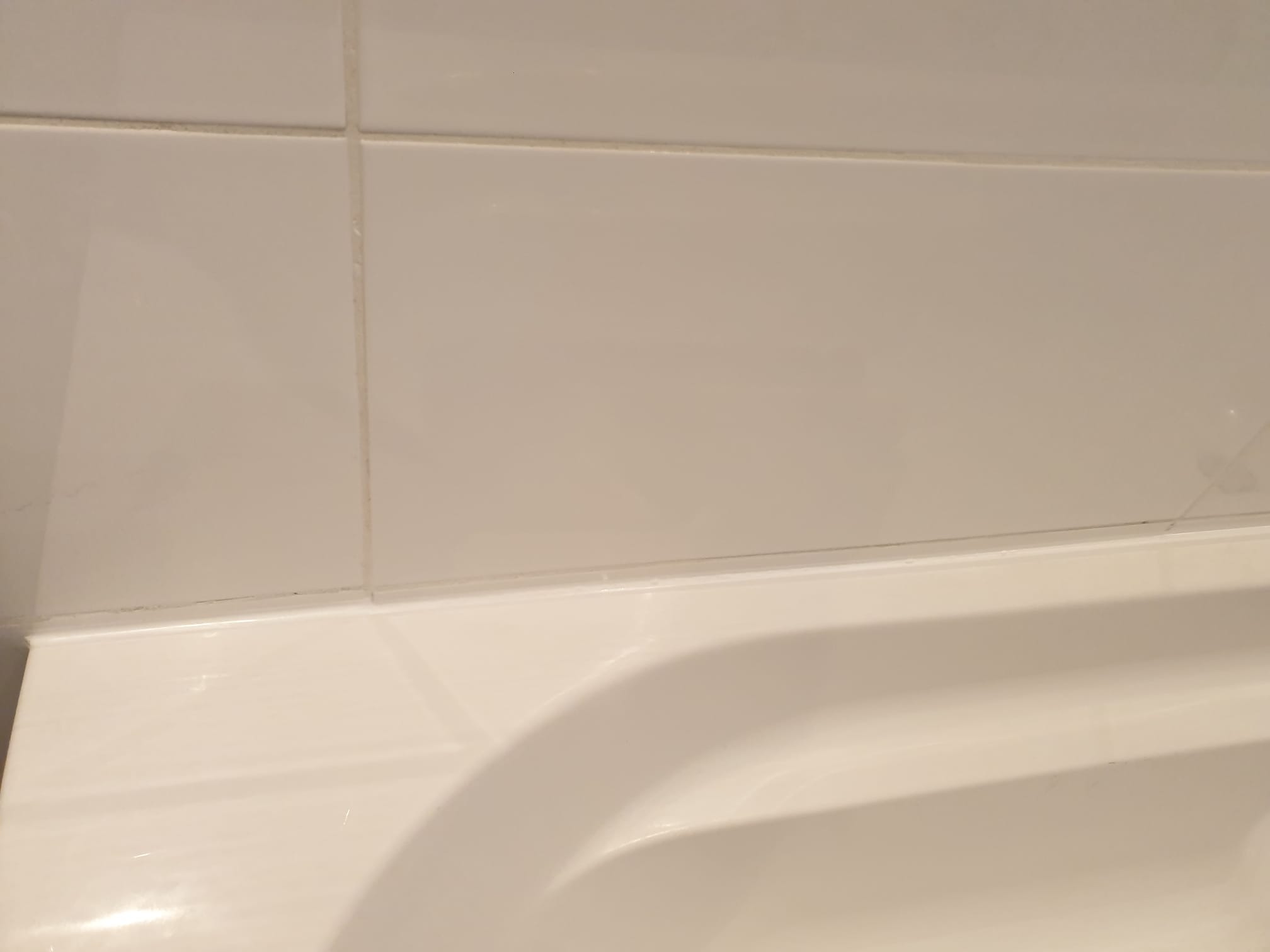 Fragment wykończonej, jasnej łazienki: białe płytki ceramiczne na ścianie nad wanną z widocznymi fugami. Minimalizm i czystość w detalu.