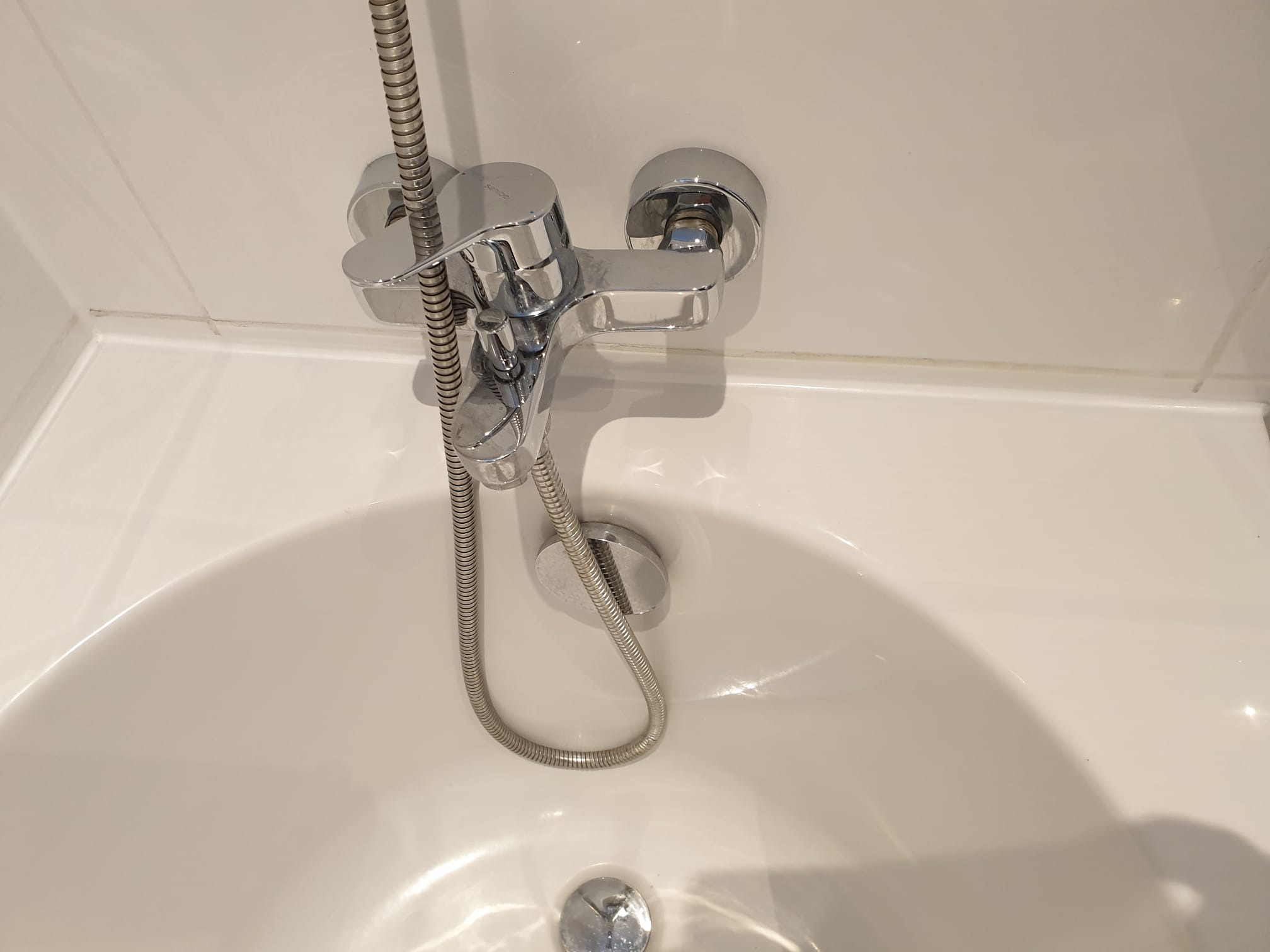 Bateria wannowa z chromowaną słuchawką prysznicową zamontowana na białej ścianie i wannie w Eberswalde. Widok z góry, minimalistyczny design.