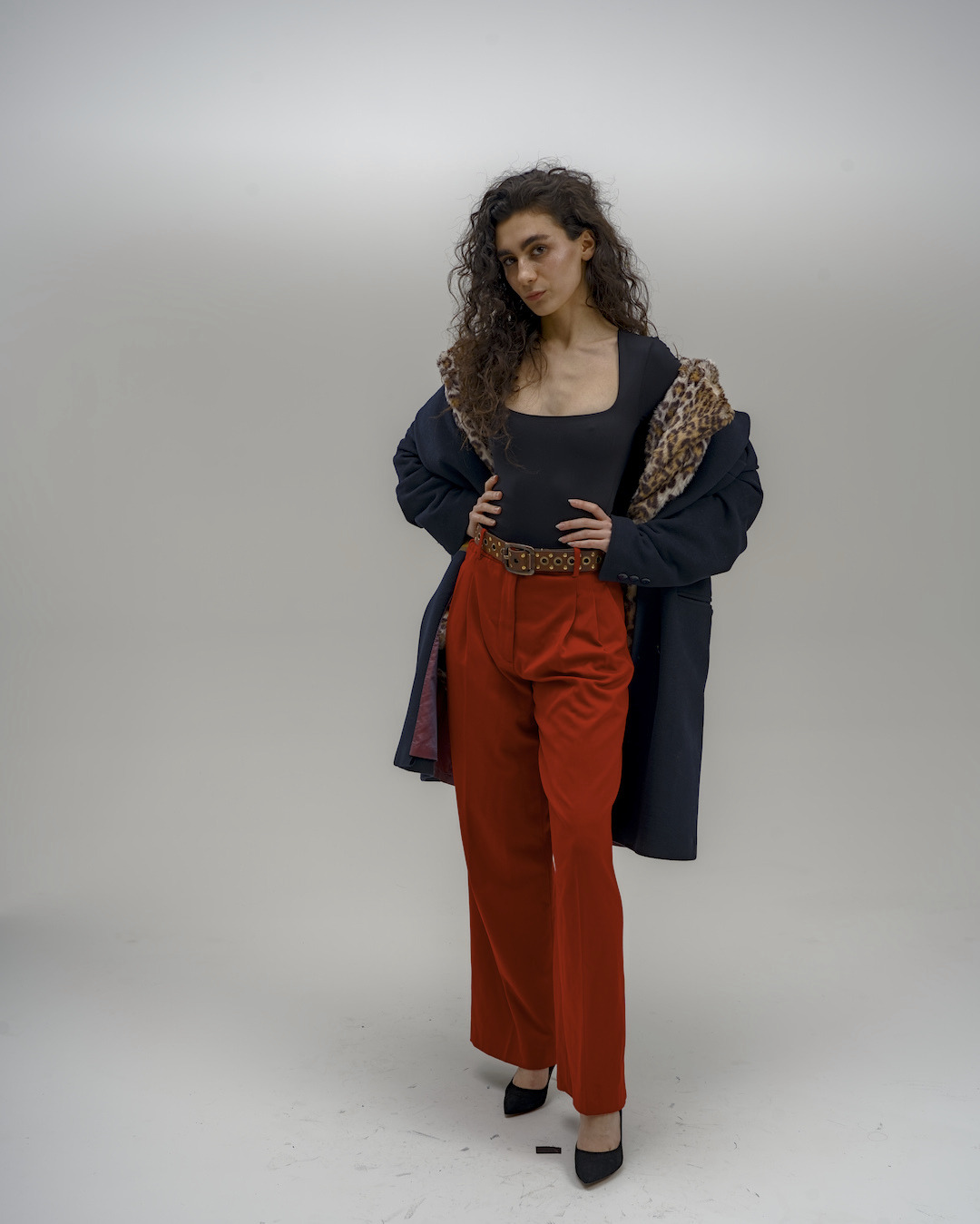 Portret kobiety w czarnym body, czerwonych spodniach i marynarce z panterkowym kołnierzem, pozującej na jasnym tle. Całość w stylu fashion.