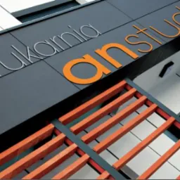 Elewacja budynku drukarni z napisem 'drukarnia anstudio' wykonanym z metalowych liter w kolorze srebrnym i pomarańczowym, widziana z dołu pod kątem.