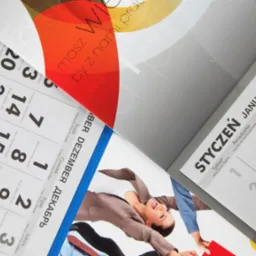 Rozłożone kalendarze firmowe z widocznymi datami i grafikami, ułożone pod kątem, ukazujące różne miesiące i style projektów.