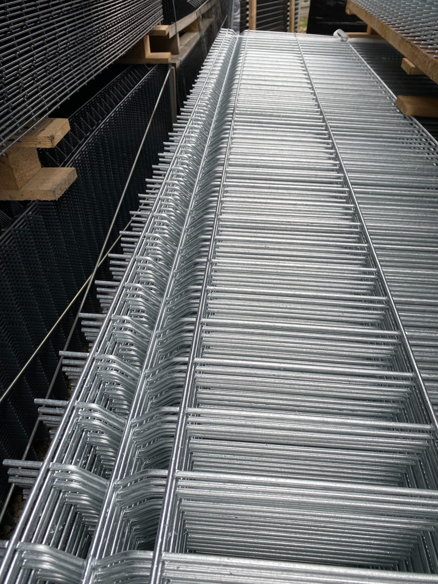 Stos ocynkowanych paneli ogrodzeniowych zgrzewanych punktowo, ułożonych na drewnianych legarach.