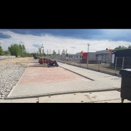 Budownictwo Drogowe Brukarstwo Robert Wieczorek - Ukończony parking z kostki brukowej w odcieniach czerwieni i szarości, z zaparkowanym skuterem. Widoczne budynki w tle i fragment ogrodzenia.