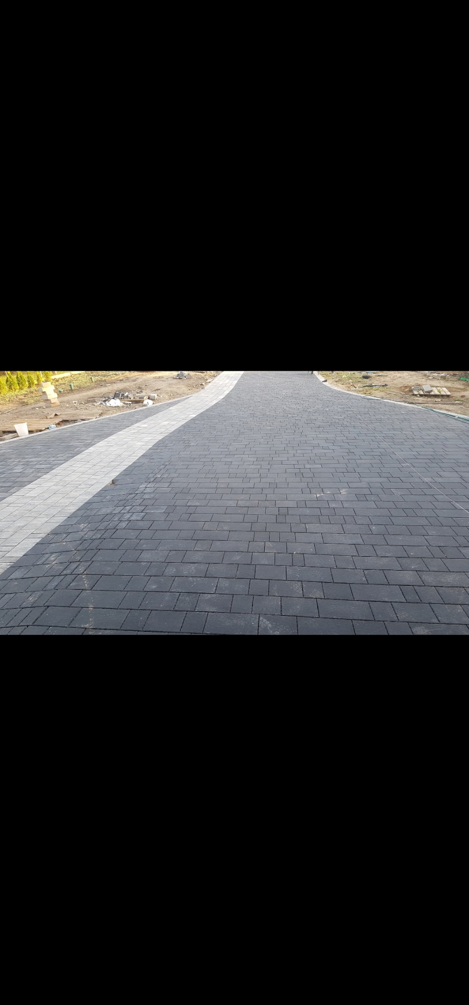 Ułożona, ciemnoszara kostka brukowa tworząca ścieżkę z jasnoszarym obramowaniem w Mińsku Mazowieckim. Widok z perspektywy.