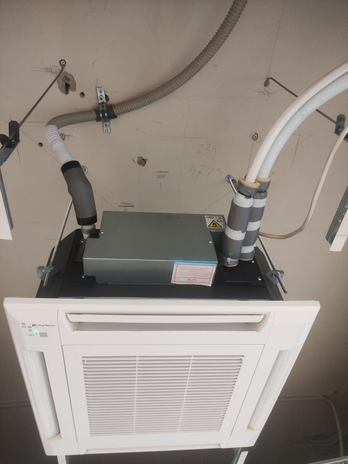 Zamontowana, kasetonowa jednostka wewnętrzna klimatyzacji Fuji Electric na suficie, z widocznymi przewodami i instalacją, surowy stan ściany z widocznymi śladami po wierceniu.