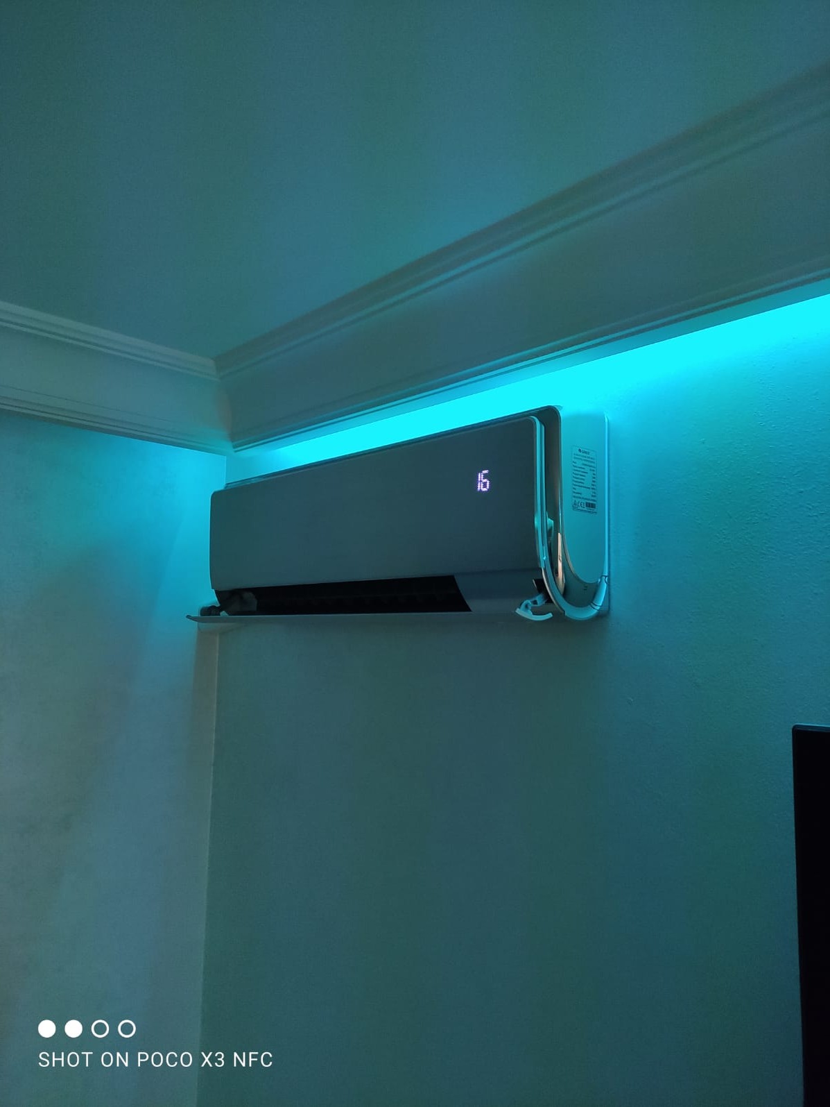 Nowoczesny klimatyzator ścienny z wyświetlaczem temperatury (16 stopni) podświetlony niebieskim światłem LED na suficie, w pomieszczeniu o jasnych ścianach.