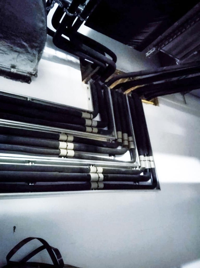 Izolowane rury instalacji chłodniczej prowadzone wzdłuż ściany, z widocznymi mocowaniami i fragmentami sufitu.