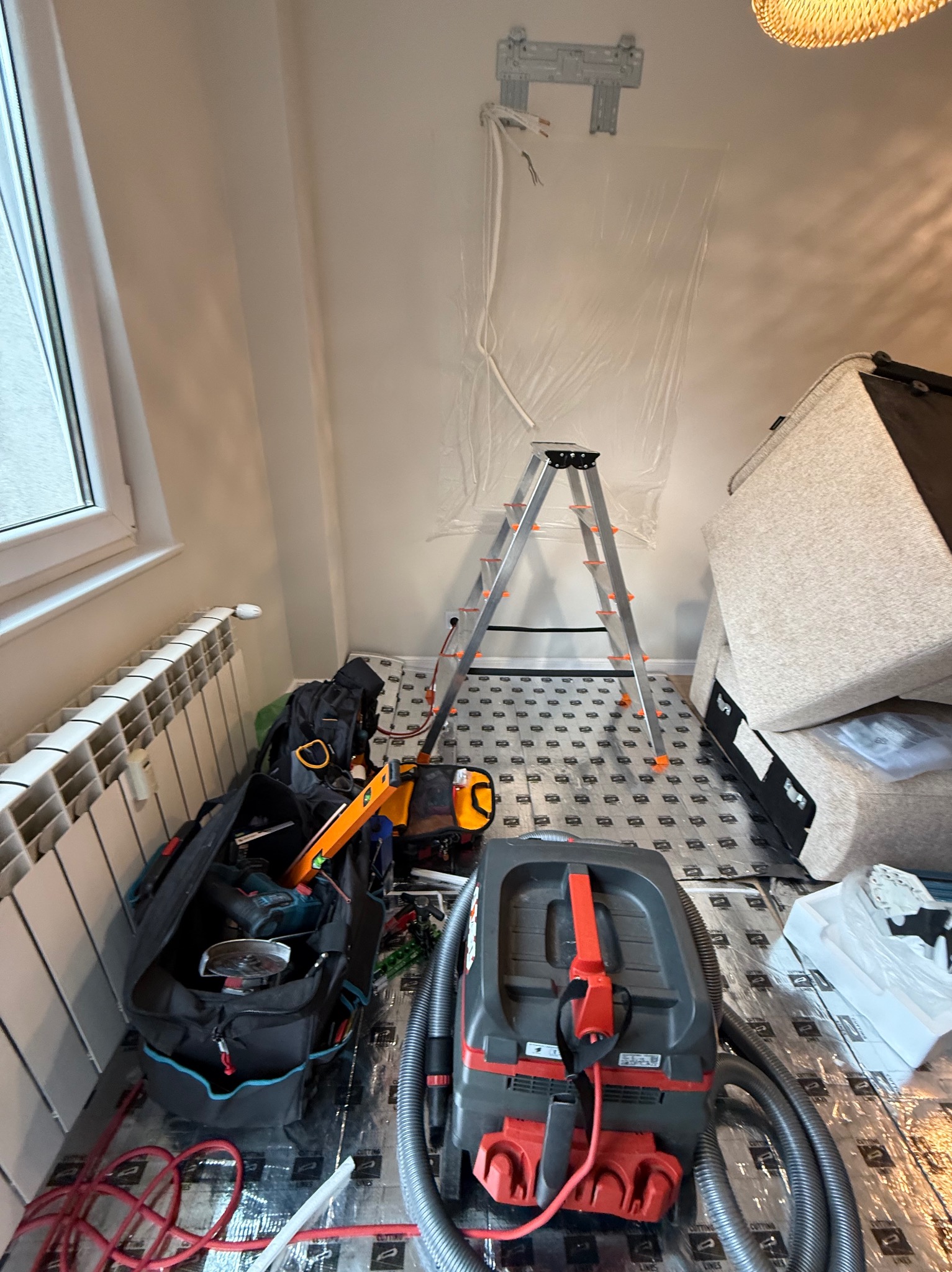 Montaż klimatyzacji w domu: widoczny uchwyt na ścianie, drabina, narzędzia i odkurzacz przemysłowy. Podłoga zabezpieczona folią ochronną.