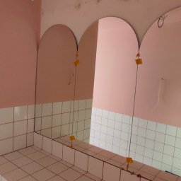 JACEK KRUK - Montaż trzech owalnych luster w łazience z różowymi ścianami i białymi kafelkami. Widoczne przyssawki montażowe i odbicie osoby robiącej zdjęcie.