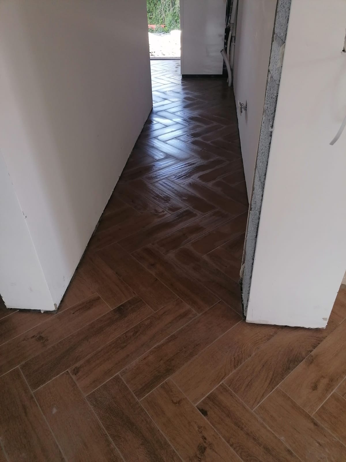 Ułożona w jodełkę podłoga z płytek imitujących drewno, widok z perspektywy wejścia, ściany w trakcie wykańczania.