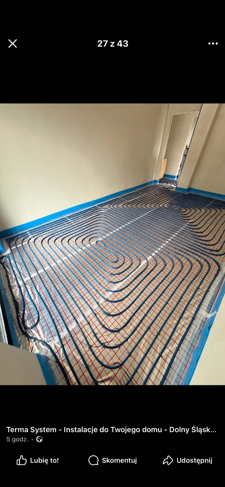 Niebieskie rury ogrzewania podłogowego ułożone spiralnie na folii z czerwoną siatką w jasnym pomieszczeniu, przygotowane do zalania wylewką. Widok z góry.