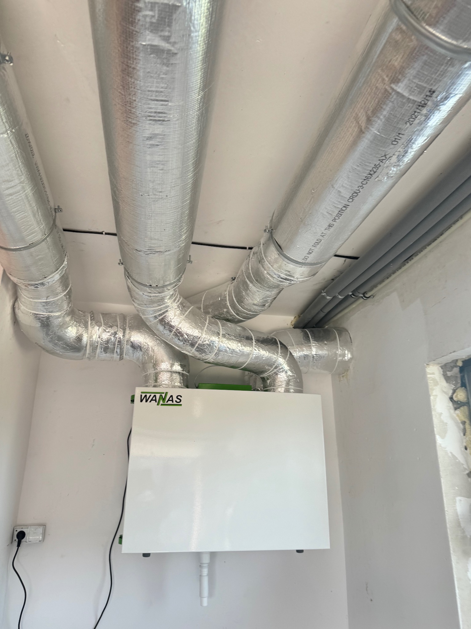Zmontowana instalacja rekuperacji WANAS z izolowanymi przewodami wentylacyjnymi w pomieszczeniu. Widoczne rury i centrala rekuperacyjna.
