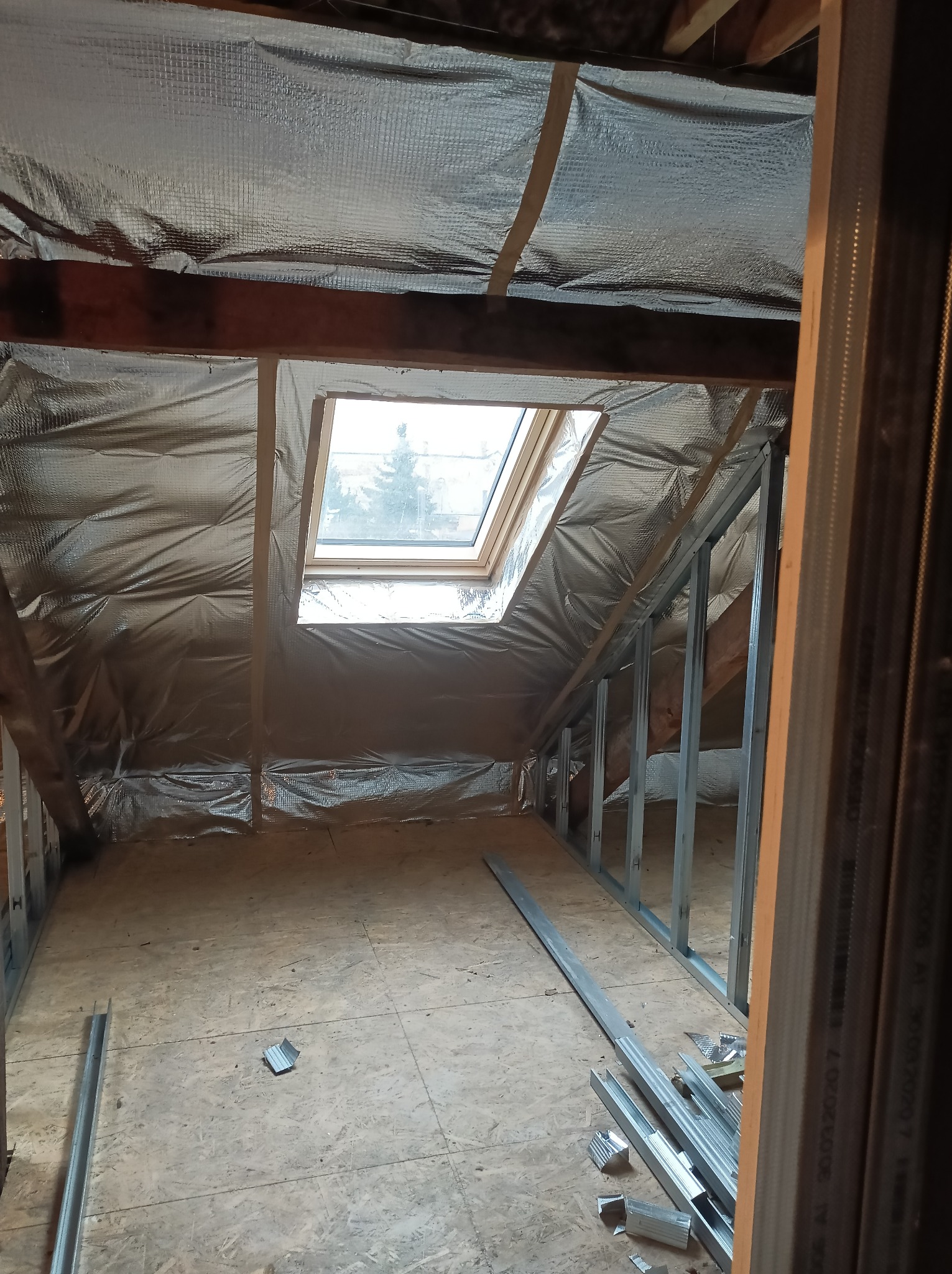Adaptacja poddasza: izolacja folią aluminiową, metalowy szkielet ścian działowych, okno dachowe. Elementy konstrukcyjne na podłodze.