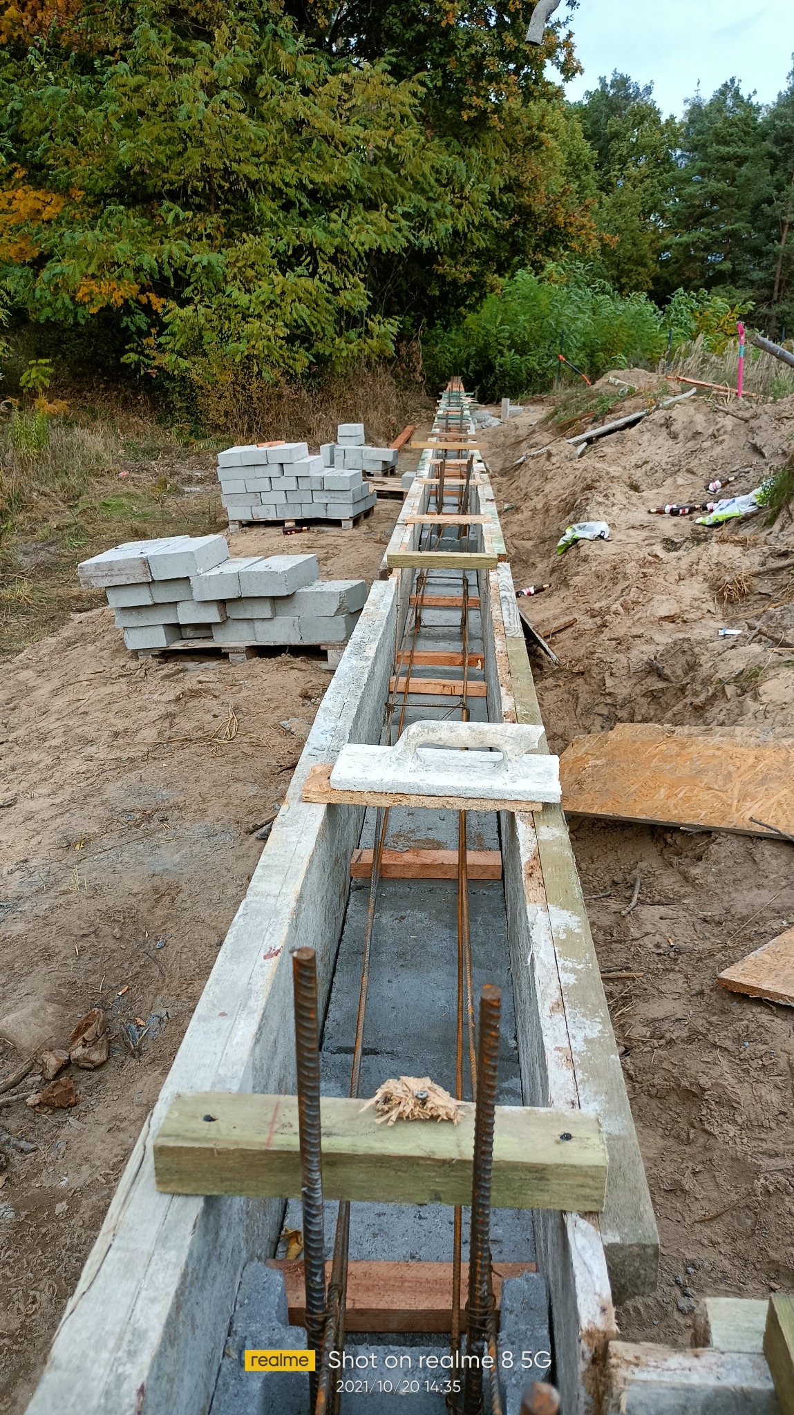 Przygotowanie fundamentów pod zabudowę balkonu: zbrojenie w szalunku betonowym, widoczne bloczki betonowe i teren budowy.
