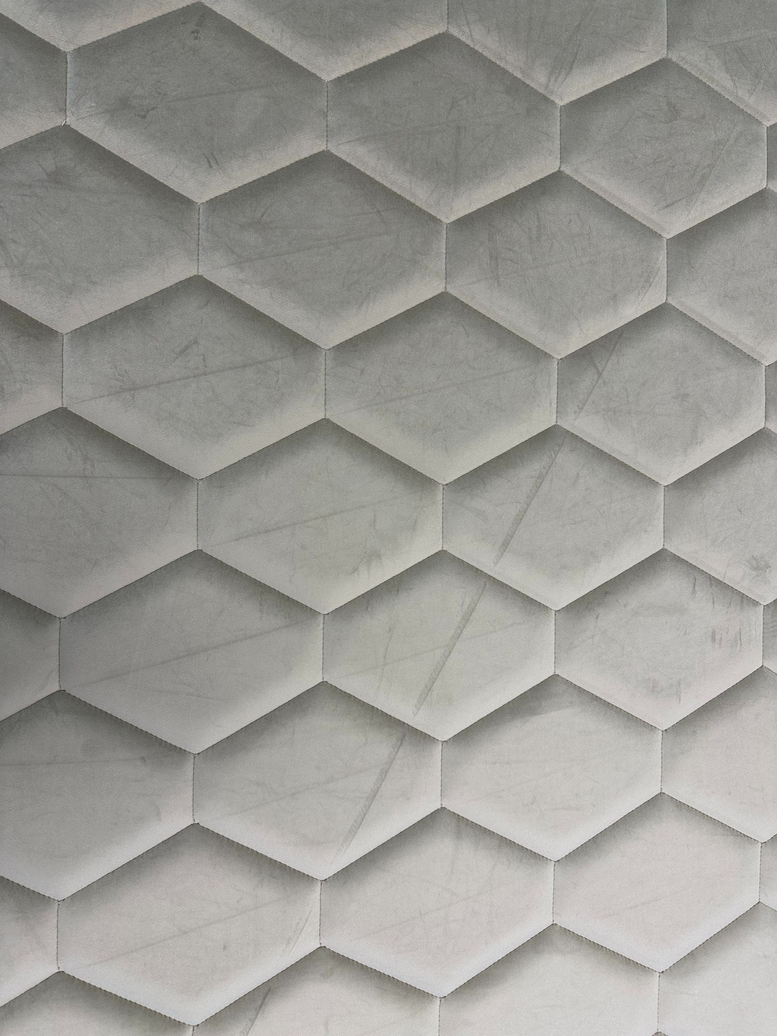 Szary panel tapicerowany z geometrycznym wzorem sześciokątów, widoczne delikatne przeszycia i faktura materiału.