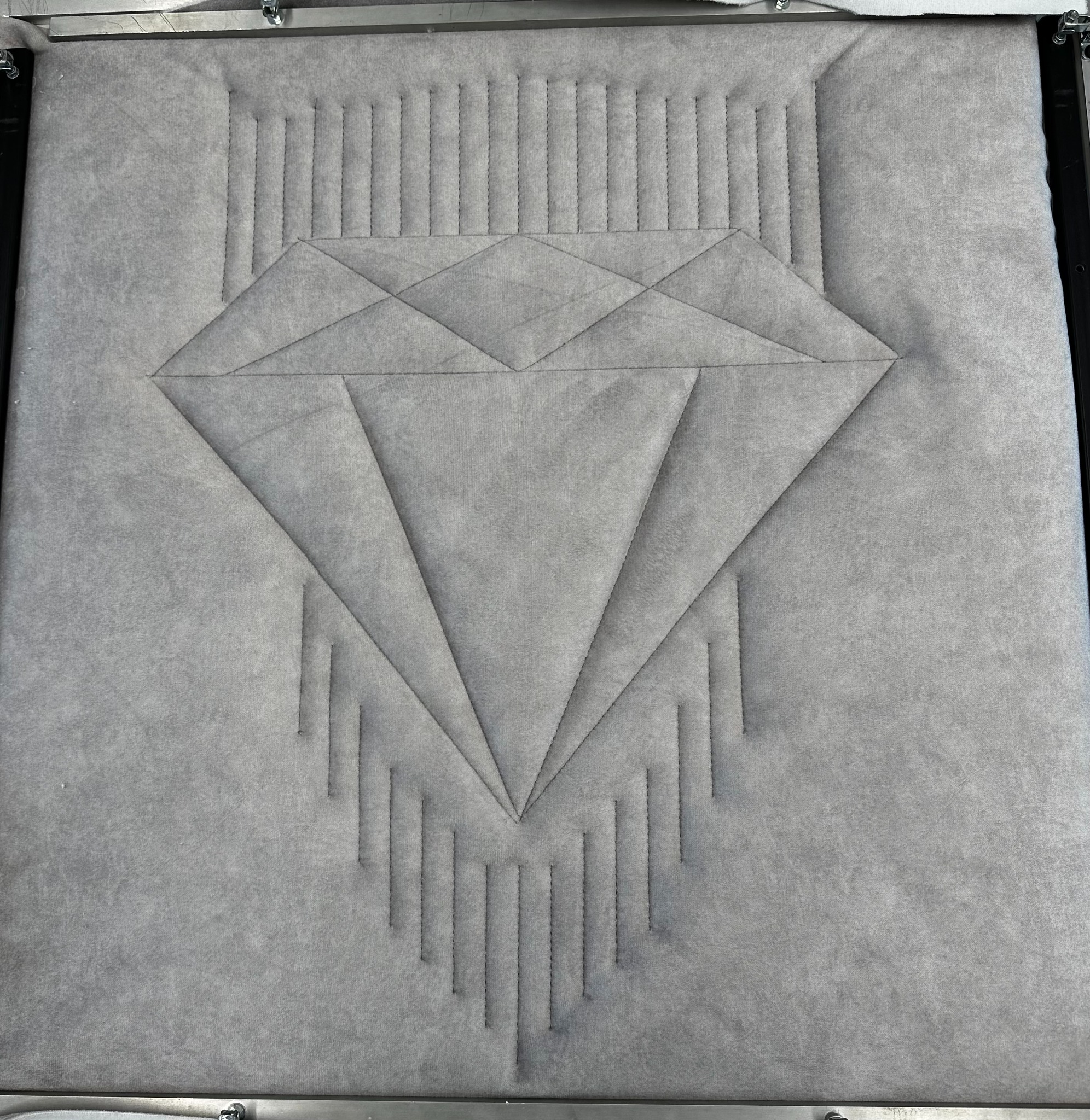 Szara tkanina z geometrycznym wzorem diamentu i pionowych linii, umieszczona w metalowej ramie.