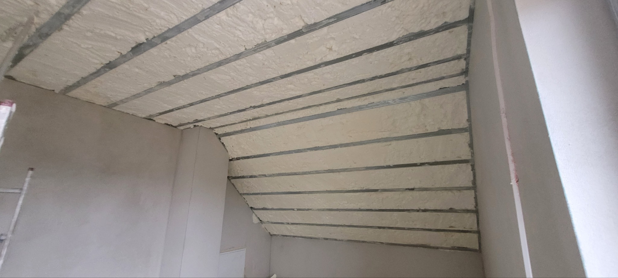 Poddasze z widoczną izolacją pianką PUR między metalowymi profilami, surowy stan wykończenia ścian.