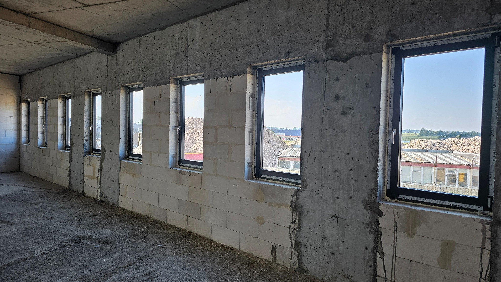 Surowy stan: Wnętrze z oknami z czarnymi ramami w trakcie montażu w surowych ścianach z betonu komórkowego i betonu. Widok na zewnątrz przez okna.