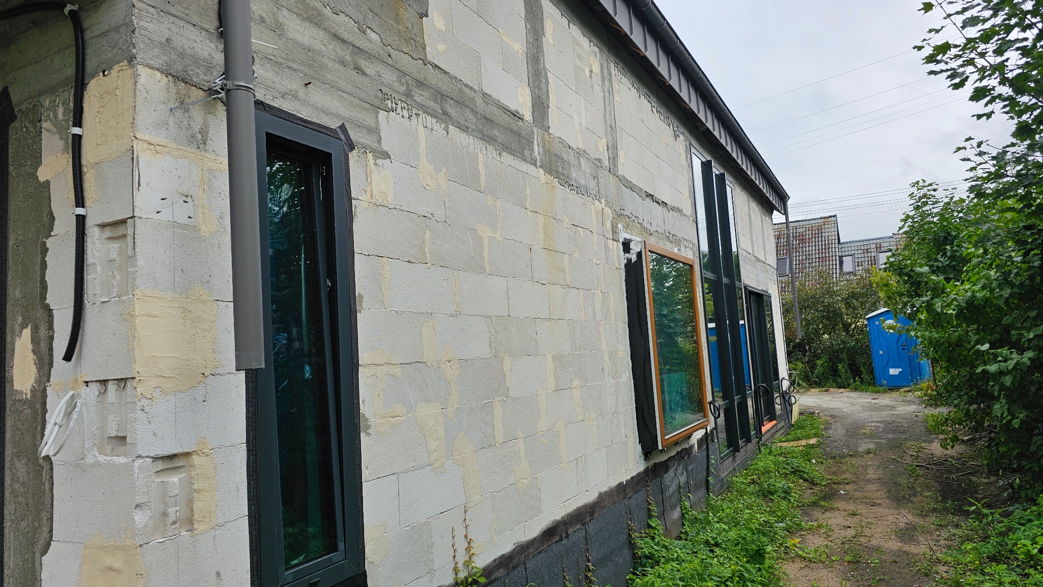 Montaż okien w surowym budynku z betonu komórkowego. Widoczne okna z różnymi kolorami ram, instalacja elektryczna, otoczenie budowy.