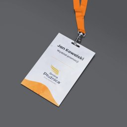 ALFABET MARKI SPÓŁKA Z OGRANICZONĄ ODPOWIEDZIALNOŚCIĄ - Identyfikator wizualny z logo i danymi osobowymi, zawieszony na pomarańczowej smyczy, leżący na szarym tle.