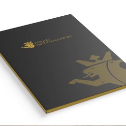 ALFABET MARKI SPÓŁKA Z OGRANICZONĄ ODPOWIEDZIALNOŚCIĄ - Czarna teczka z logo Powiatu Inowrocławskiego w kolorze złotym, widoczna z perspektywy, leżąca na białym tle.