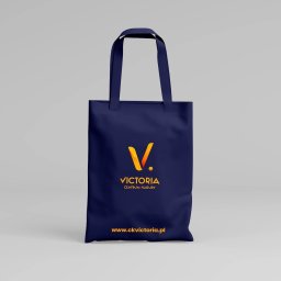 ALFABET MARKI SPÓŁKA Z OGRANICZONĄ ODPOWIEDZIALNOŚCIĄ - Granatowa torba bawełniana z pomarańczowym logo Victoria Centrum Kultury i adresem strony internetowej, na jasnoszarym tle.