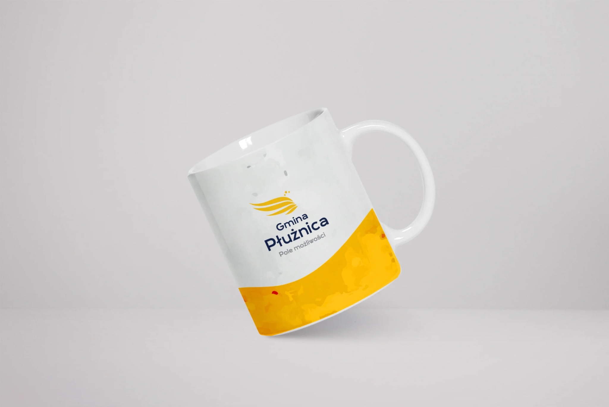 Biały kubek z nadrukiem logo i napisem 'Gmina Płużnica. Pole możliwości' na jasnoszarym tle.