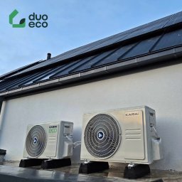 Duoeco Sp. z o.o. - Dwa zewnętrzne agregaty klimatyzacji Kaisai ECO na betonowych podstawach, zamontowane na ścianie budynku z panelami fotowoltaicznymi na dachu.