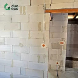 Ściana z betonu komórkowego z przygotowaną instalacją elektryczną. Widoczne kable i puszki instalacyjne. Budynek w trakcie budowy lub remontu.