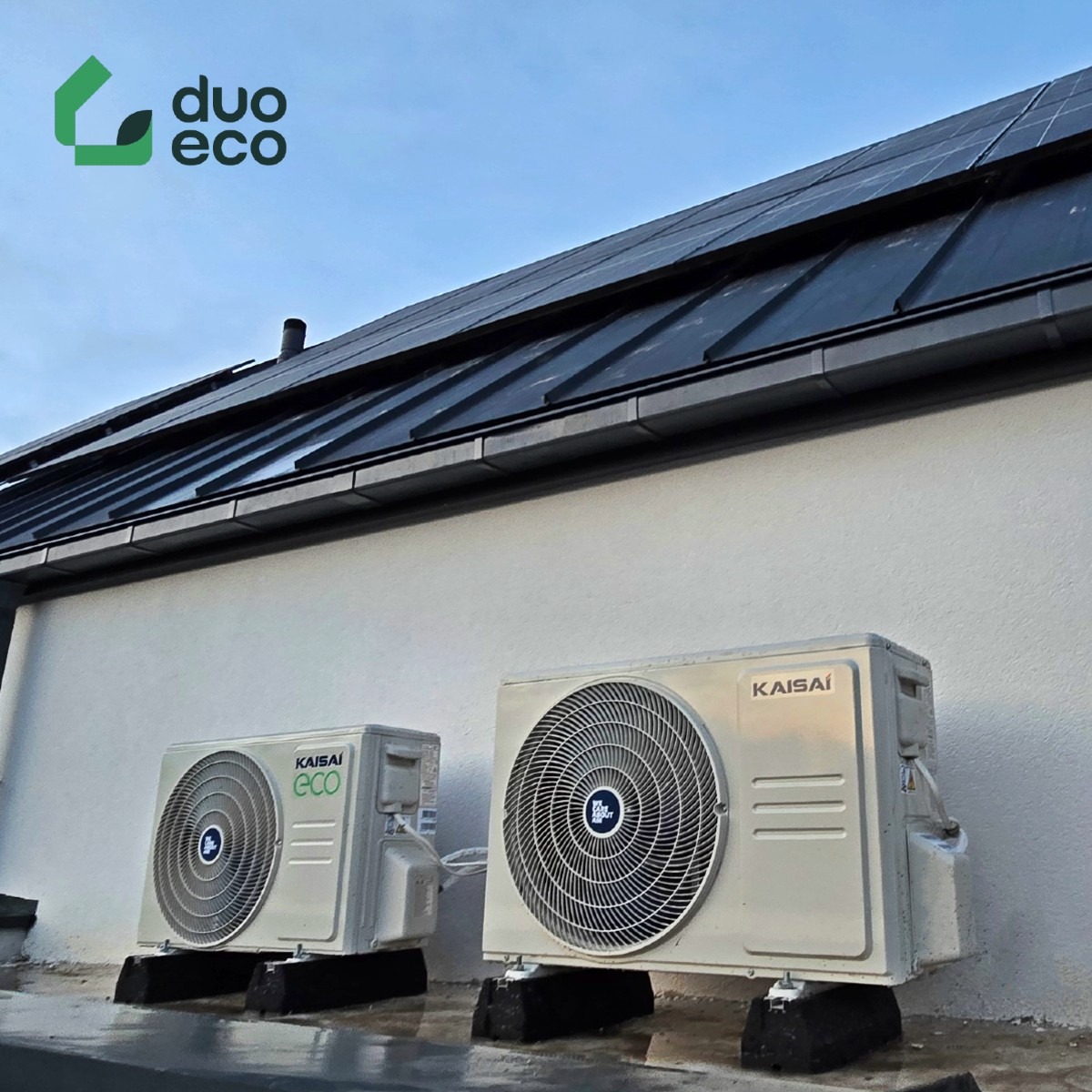 Dwa zewnętrzne agregaty klimatyzacji Kaisai ECO na betonowych podstawach, zamontowane na ścianie budynku z panelami fotowoltaicznymi na dachu.