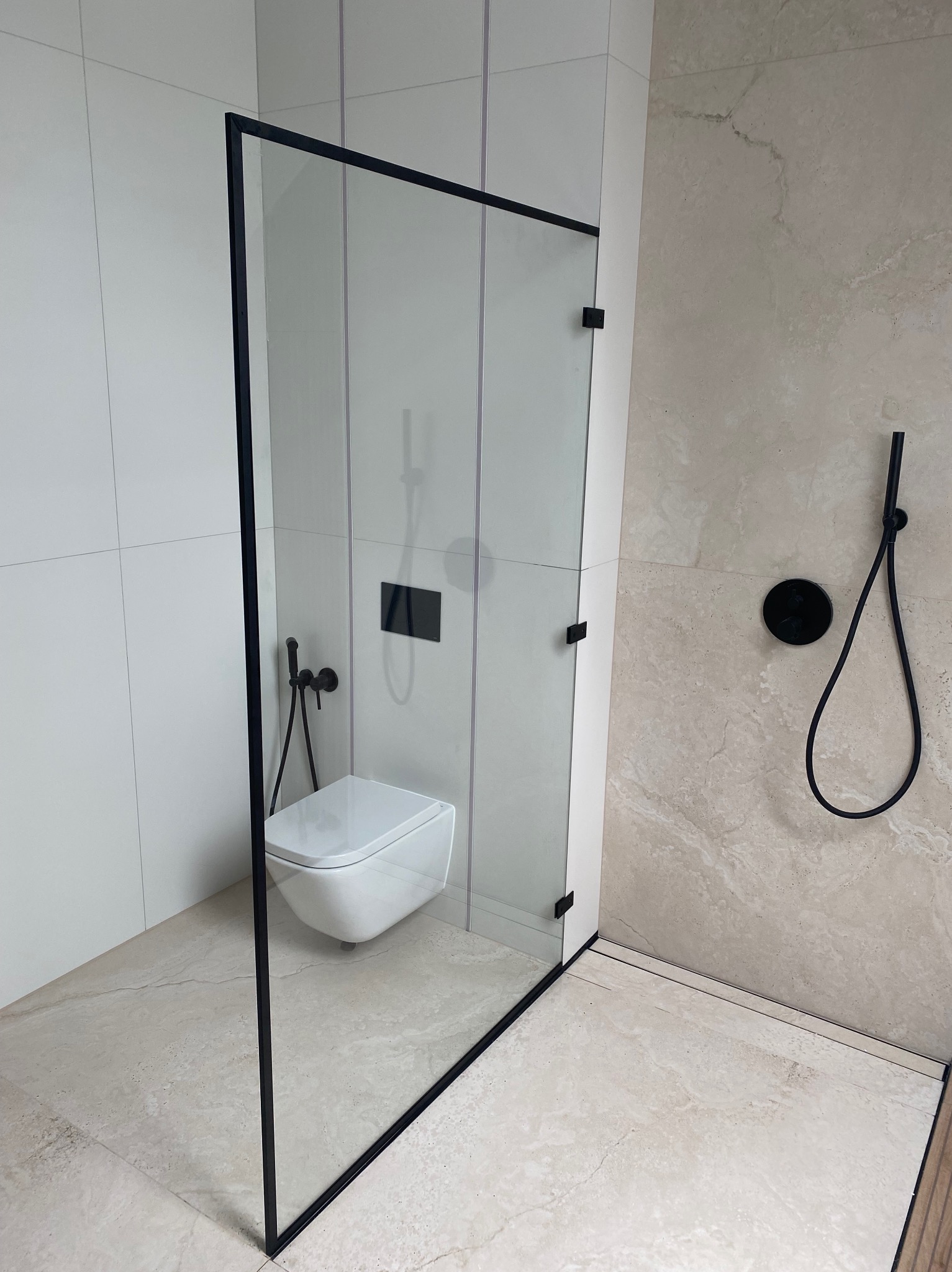 Nowoczesna kabina prysznicowa ze szkła hartowanego w czarnej ramie, minimalistyczna armatura w łazience z beżowymi płytkami.
