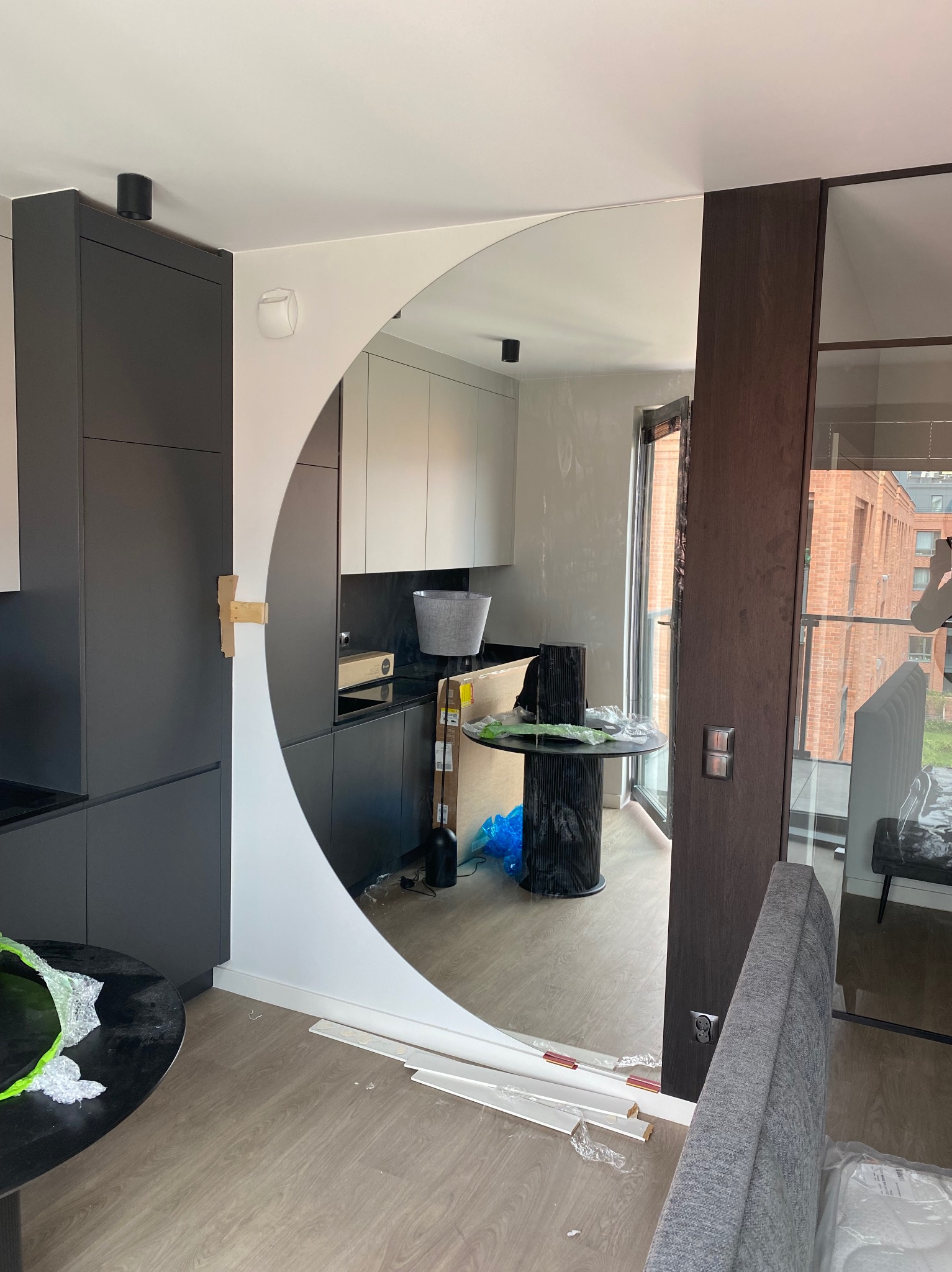 Montaż lustra w kształcie półksiężyca w kuchni z ciemnymi szafkami. Widoczne elementy montażowe i częściowo zamontowane listwy przypodłogowe.