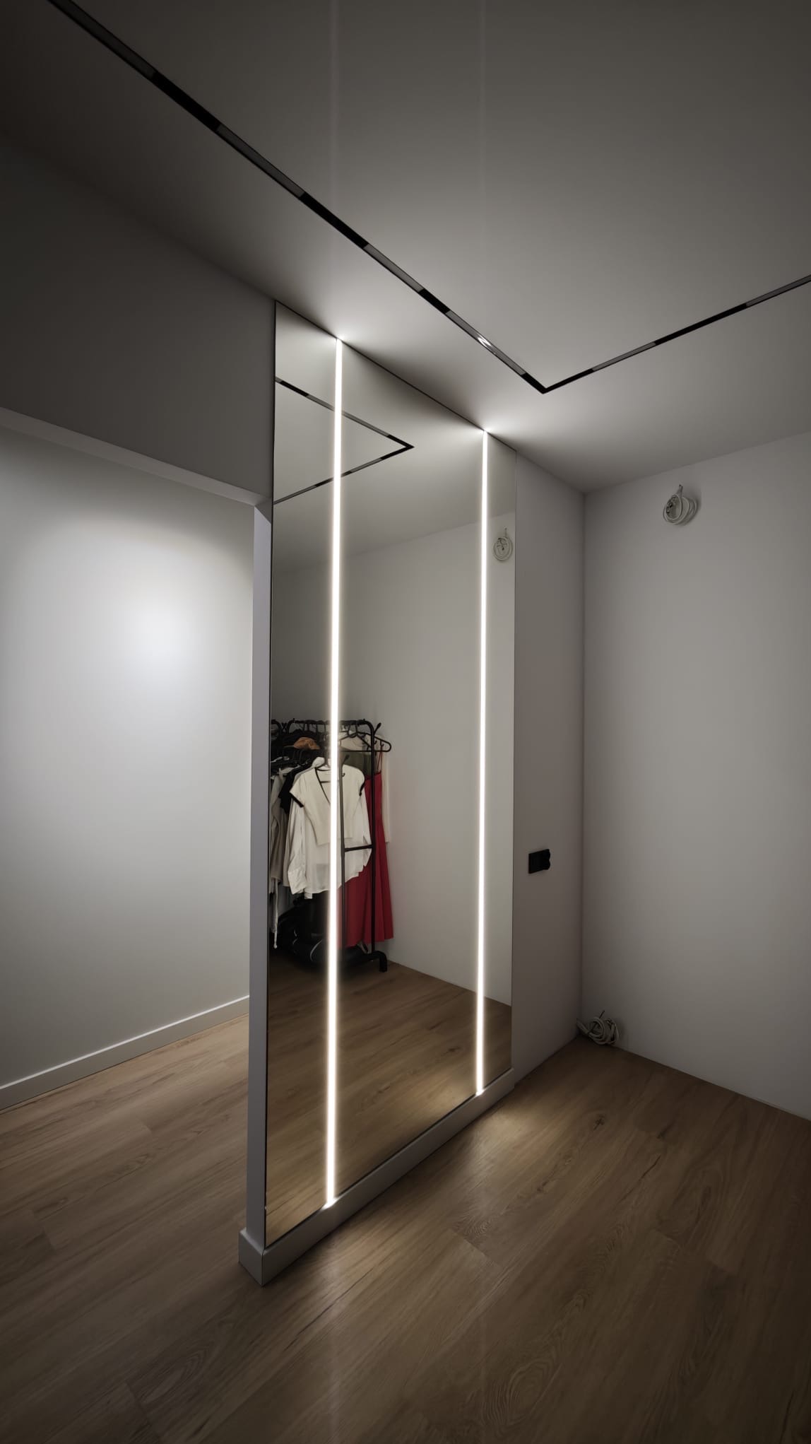 Nowoczesne drzwi przesuwne z lustrem i oświetleniem LED w minimalistycznym wnętrzu. Widoczna garderoba w odbiciu lustrzanym.