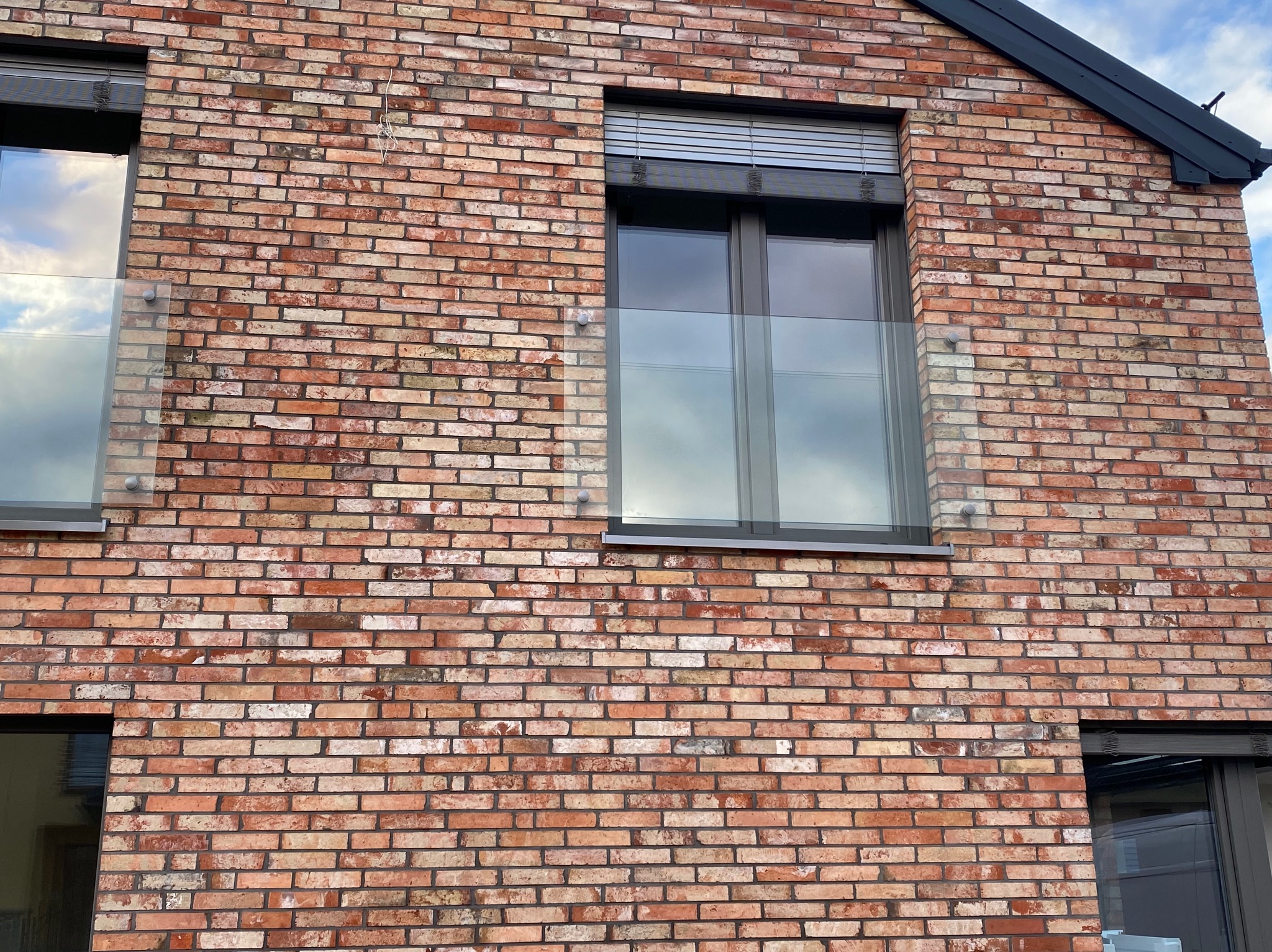 Ceglana elewacja budynku z oknami zabezpieczonymi szklanymi balustradami. Widoczne mocowania balustrad do ściany. Okna z żaluzjami.