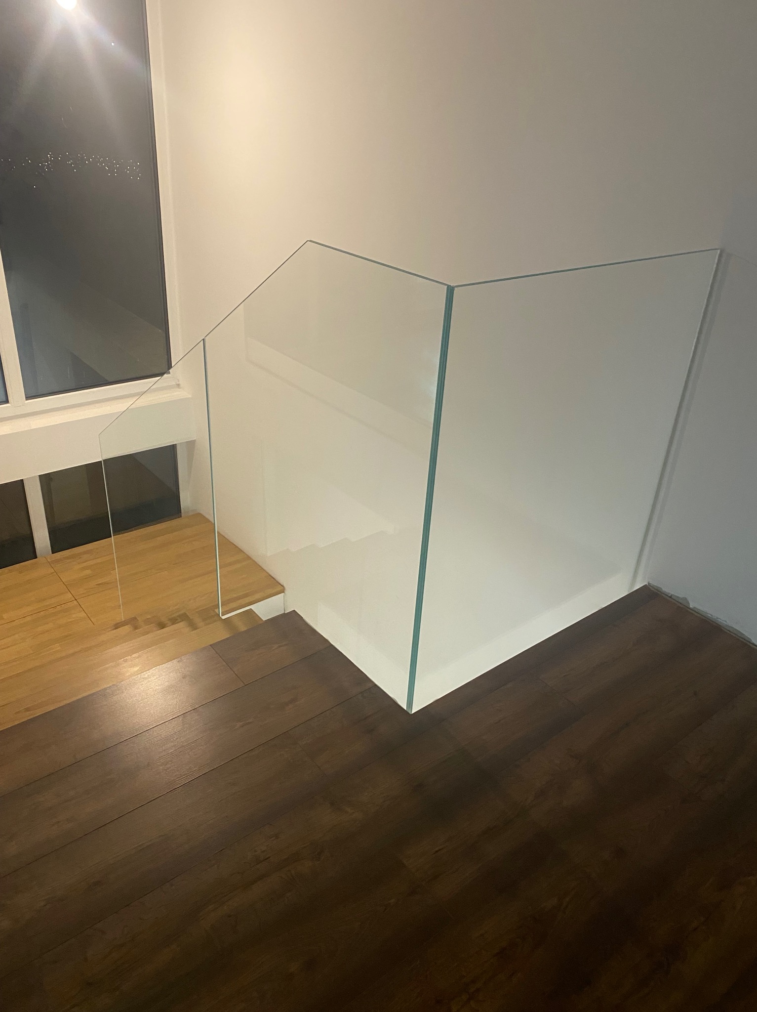 Szklana balustrada na schodach z drewnianymi stopniami, widok z góry, minimalistyczny design, jasne wnętrze, nowoczesne wykończenie.