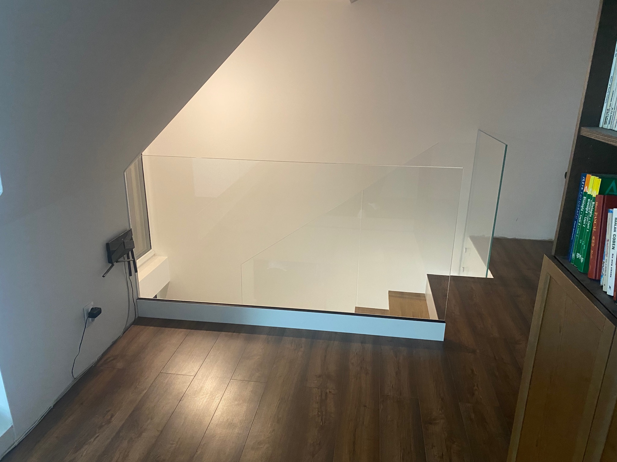 Szklana balustrada zabezpieczająca schody w nowoczesnym domu. Minimalistyczny design z drewnianą podłogą i białymi ścianami. Widok z góry na schody.