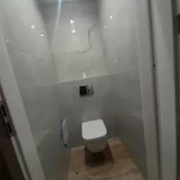 Nowoczesna, wykończona łazienka z podwieszaną toaletą, szarymi płytkami ściennymi i drewnopodobną podłogą. Widoczne niedokończone podłączenia elektryczne.