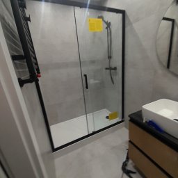 Perfect Marcin Roguski - Nowoczesna łazienka po remoncie: kabina prysznicowa z czarną ramą, grzejnik drabinkowy i umywalka nablatowa. Minimalistyczny design, szare płytki.