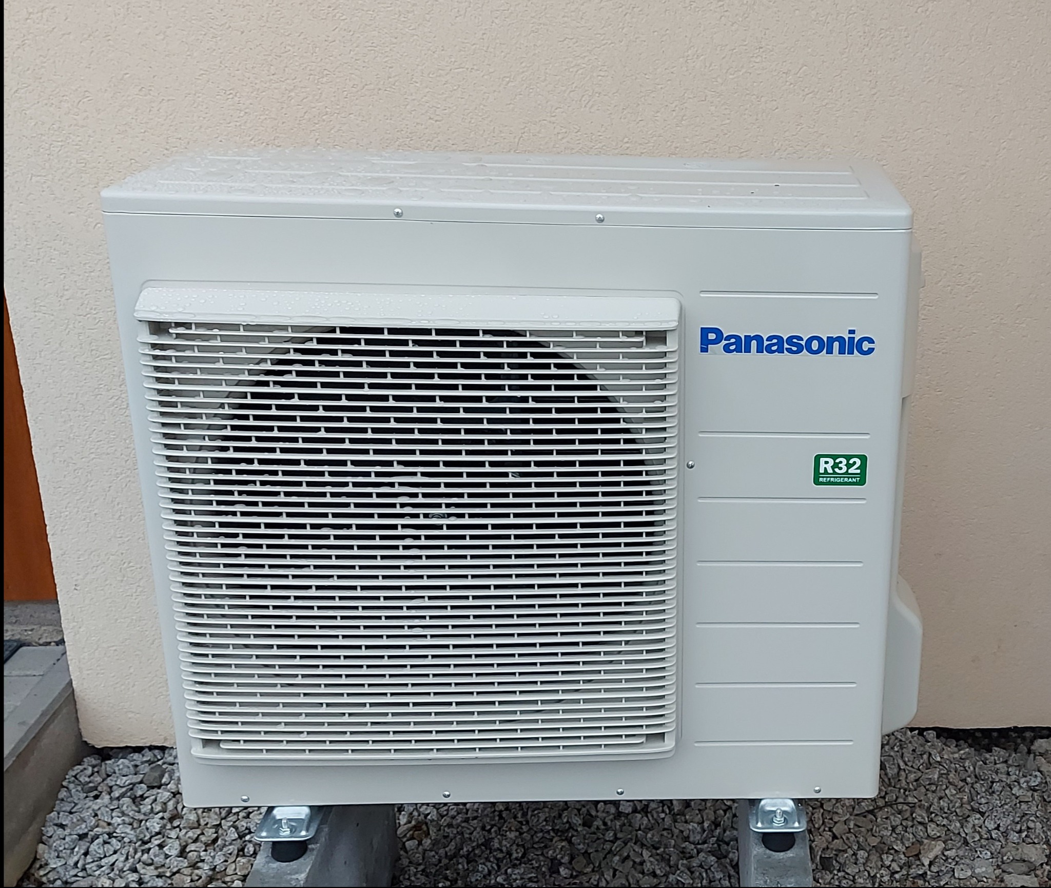 Zewnętrzna jednostka klimatyzacji Panasonic na betonowych podstawach, widoczne krople wody na obudowie i logo R32 refrigerant.