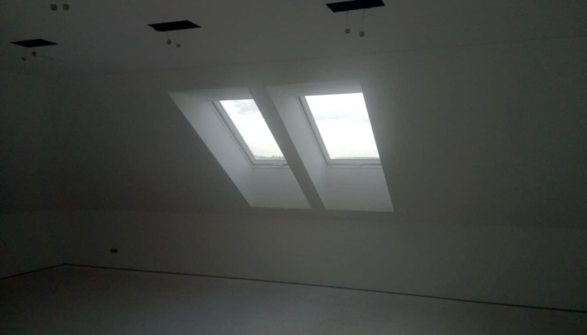 Poddasze z dwoma oknami dachowymi, świeżo pomalowane na biało, widoczne przygotowane otwory na oświetlenie sufitowe.