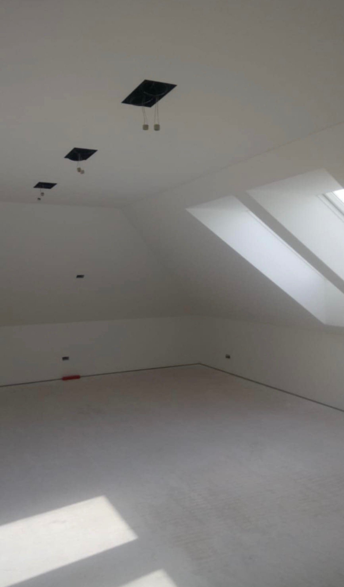 Poddasze po remoncie, widoczne okna dachowe, świeżo pomalowane ściany na biało i przygotowane otwory pod oświetlenie punktowe w suficie.