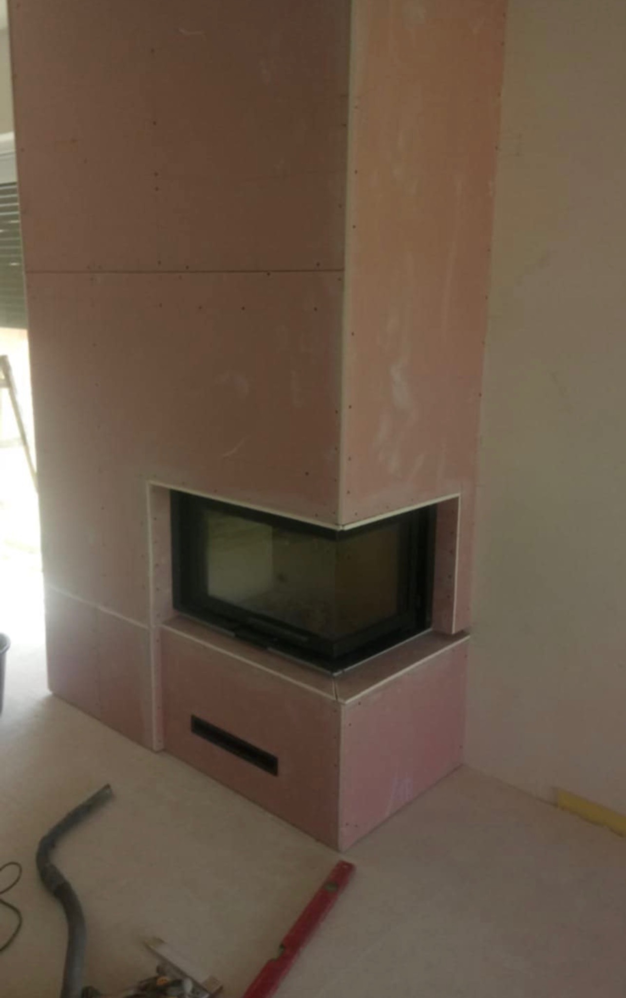 Obudowa kominka z płyty kartonowo-gipsowej w trakcie montażu, widoczne narzędzia i poziomica na podłodze.